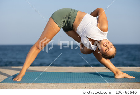 Sportive girl practicing triangle pose of yoga on seashore Sportive girl practicing triangle pose of yoga on seashore 136460640
