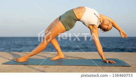 On windy day young slender woman does yoga near sea doing Chamatkarasana On windy day young slender woman does yoga near sea doing Chamatkarasana 136460753