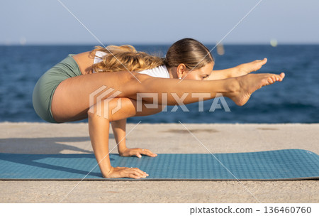 On windy day young slender woman does yoga near sea doing titibasana On windy day young slender woman does yoga near sea doing titibasana 136460760
