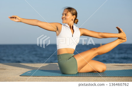 Flexible girl practicing lord of the fishes pose of yoga on seashore 136460762