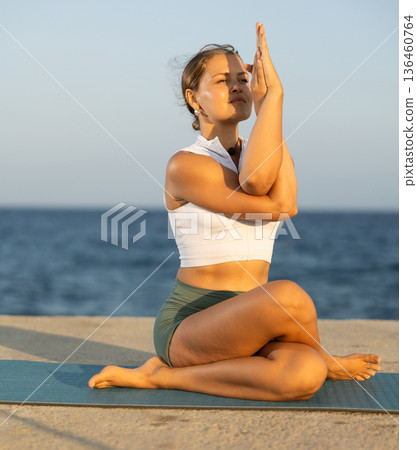 Relaxed girl performing Ardha Matsyendrasana position yoga training on beach Relaxed girl performing Ardha Matsyendrasana position yoga training on beach 136460764