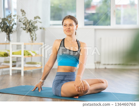 Young woman practicing parivritta sukhasana yoga pose 136460768