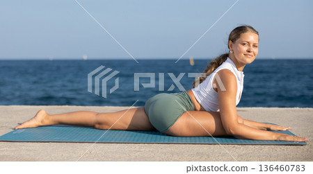 Sportive girl practicing pigeon pose of yoga on seashore 136460783