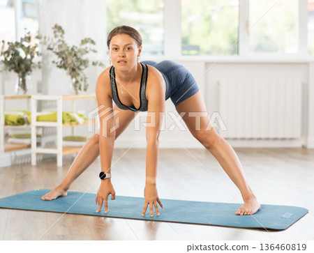 Sportive girl practicing wide legged forward bend pose of yoga in light room 136460819