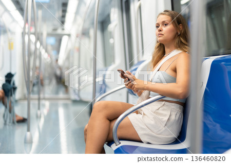 Young woman is sitting in subway car with phone, getting to work, school. 136460820