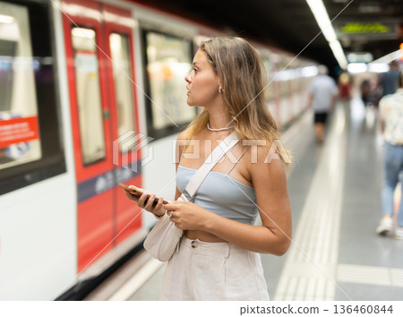 Young girl standing in platform with phone in hand Young girl standing in platform with phone in hand 136460844