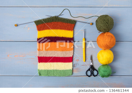 Working wooden needlework table with balls of thread and knitting needles, scissors, knitted scarf in the process, crochet Working wooden needlework table with balls of thread and knitting needles, scissors, knitted scarf in the process, crochet 136461344