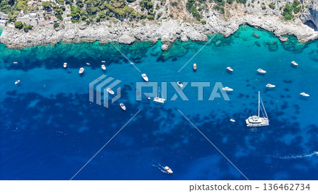 Serene Mediterranean seascape with numerous boats resting in crystal clear waters near rocky coastline Serene Mediterranean seascape with numerous boats resting in crystal clear waters near rocky coastline 136462734