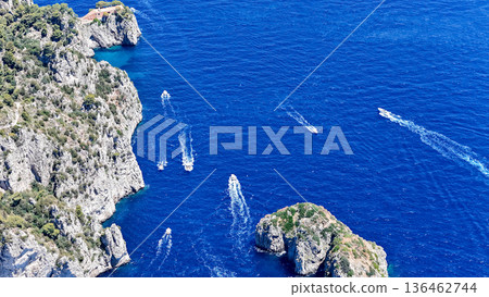 Vibrant boats cruise through the sparkling waters of a stunning coastal landscape filled with cliffs and lush greenery 136462744