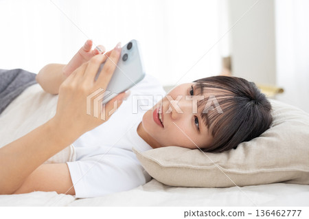 一位年輕的女士在床上操縱智能手機 一位年輕的女士在床上操縱智能手機 136462777