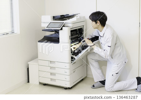 A young Japanese man maintaining a copy machine 136463287