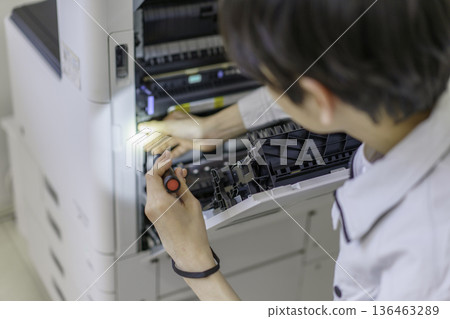 Close-up of a young Japanese man's hands performing maintenance on a copy machine Close-up of a young Japanese man's hands performing maintenance on a copy machine 136463289