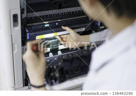 Close-up of a young Japanese man's hands performing maintenance on a copy machine 136463290
