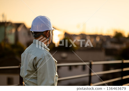 The back of a veteran construction manager illuminated by the setting sun 136463679