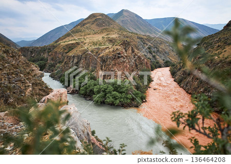 Two rivers with clear and muddy water merge in a mountainous canyon landscape. Meeting of waters phenomenon for ecology and travel concept. 136464208