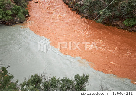 Confluence of two rivers with distinct color mixing on water surface. Natural phenomenon of merging muddy brown and clear gray waters. Confluence of two rivers with distinct color mixing on water surface. Natural phenomenon of merging muddy brown and clear gray waters. 136464211