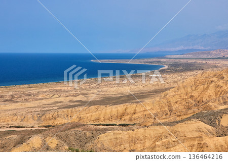 Aksai canyon view of the deep blue lake bordering arid red rock formations and mountains. Kyrgyzstan landscape for travel and geology concept. 136464216