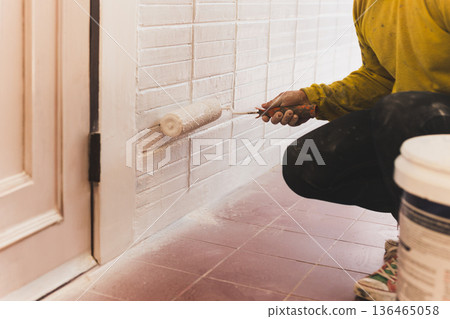 Man painting a house wall with roller in white color. 136465058