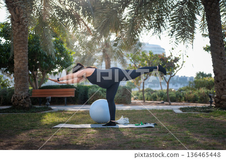 Woman Doing Balance Exercise With Stability Ball In Park For Outdoor Fitness And Flexibility Woman Doing Balance Exercise With Stability Ball In Park For Outdoor Fitness And Flexibility 136465448