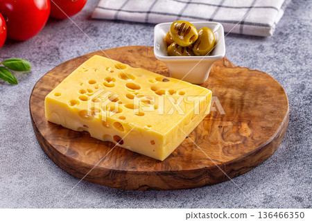 Block of Swiss cheese on a wooden cutting board with grilled olives and fresh tomatoes Block of Swiss cheese on a wooden cutting board with grilled olives and fresh tomatoes 136466350