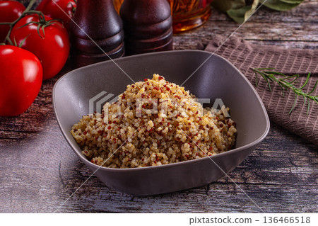 Healthy cooked tri-color quinoa in a bowl with fresh tomatoes and rosemary on a rustic wooden table 136466518