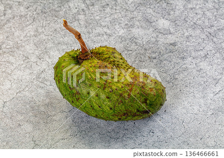 One whole raw soursop fruit, or graviola, isolated on a textured background. One whole raw soursop fruit, or graviola, isolated on a textured background. 136466661