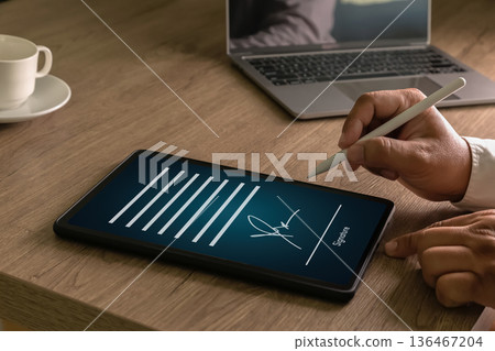 Businessman Electronic Signing document on a tablet with a stylus laptop representing secure e signature, contract approval, signs and paperless workflow. 136467204