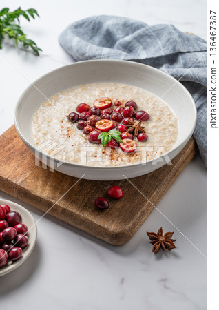 Oatmeal with cranberry, cinnamon and spicy in a plate on a wooden board on a marble background 136467387