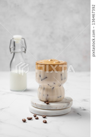 Dalgona coffee. Whipped instant iced coffee in a glass with coffee beans and bottle on a marble background. Dalgona coffee. Whipped instant iced coffee in a glass with coffee beans and bottle on a marble background. 136467392
