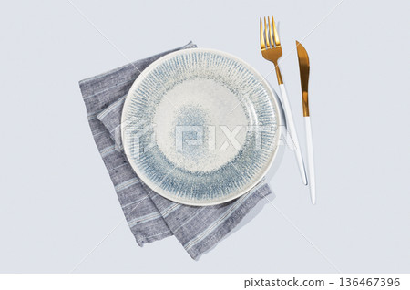 A ceramic blue plate with a linen napkin and cutlery on a light isolated background. A ceramic blue plate with a linen napkin and cutlery on a light isolated background. 136467396