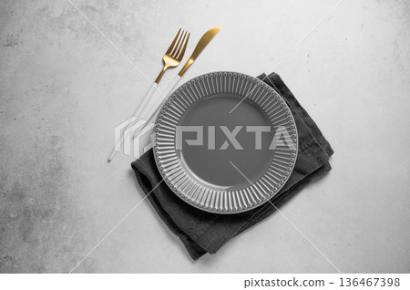 A ceramic dark gray plate with a cutlery and linen napkin on a concrete background. A ceramic dark gray plate with a cutlery and linen napkin on a concrete background. 136467398