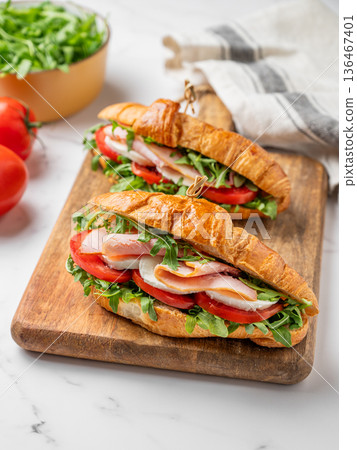 Two croissant sandwiches with ham, mozzarella cheese and arugula on a wooden board Two croissant sandwiches with ham, mozzarella cheese and arugula on a wooden board 136467401