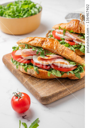 Two croissant sandwiches with ham, mozzarella cheese and arugula on a wooden board Two croissant sandwiches with ham, mozzarella cheese and arugula on a wooden board 136467402
