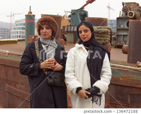 Two Women in Winter Coats at Industrial Shipyard Pier, Casual Friends Portrait Two Women in Winter Coats at Industrial Shipyard Pier, Casual Friends Portrait 136472188