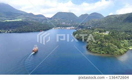 The Hakone Pirate Ship sailing gracefully across Lake Ashi and the majestic mountain range of the outer rim | Spectacular views of the resort area with a vast lake and sky The Hakone Pirate Ship sailing gracefully across Lake Ashi and the majestic mountain range of the outer rim | Spectacular views of the resort area with a vast lake and sky 136472604