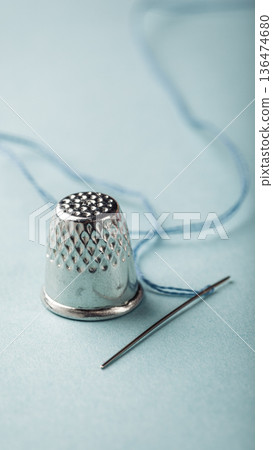 Silver thimble and needle with blue thread on soft pastel background for sewing enthusiasts Silver thimble and needle with blue thread on soft pastel background for sewing enthusiasts 136474680