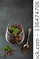 Glass container filled with roasted coffee beans and fresh mint leaves on dark textured surface 136474706