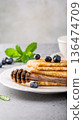 Stack of fluffy pancakes with blueberries and honey drizzled on a white plate with mint leaves 136474709