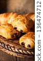 Freshly baked chocolate croissants arranged on a rustic wooden platter with warm tones 136474712