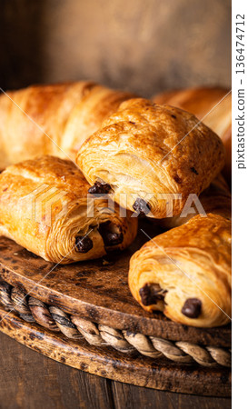 Freshly baked chocolate croissants arranged on a rustic wooden platter with warm tones 136474712