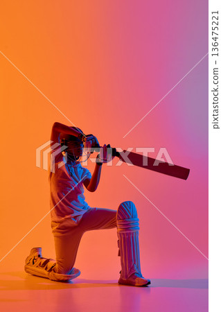 Cricket player kneeling with bat grounded in neon studio light background. 136475221