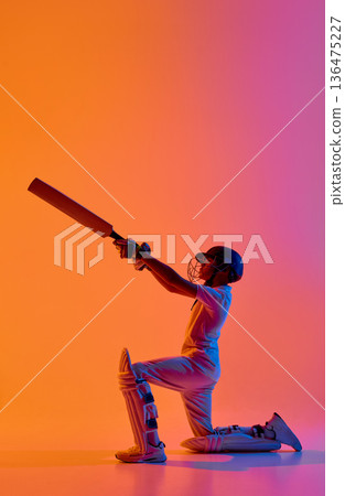 Cricket player kneeling raising bat upward in dramatic gradient light Cricket player kneeling raising bat upward in dramatic gradient light 136475227