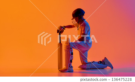 Cricket player kneeling holding bat against bold orange purple background. Cricket player kneeling holding bat against bold orange purple background. 136475228