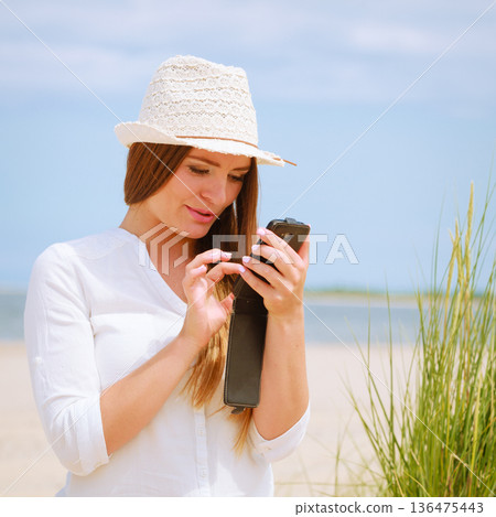 Woman on beach texting on smartphone. 136475443