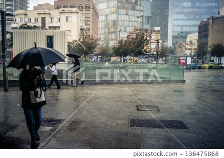 Pedestrians walk with umbrellas in the rain Pedestrians walk with umbrellas in the rain 136475868