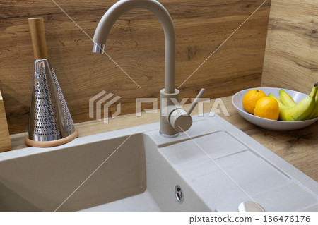 Clean lines create a modern kitchen atmosphere, with a stylish faucet next to a trendy bowl of fresh fruits and natural wood surroundings 136476176