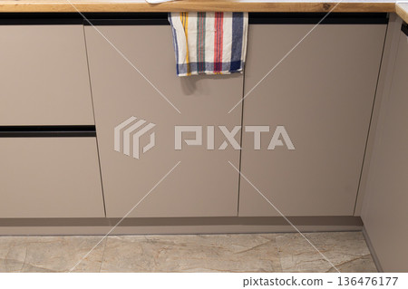 Stylish kitchen area featuring smooth cabinets and a vibrant towel hanging cheerfully, perfect for cooking or entertaining friends 136476177