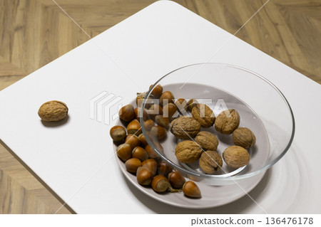A variety of nuts sit on a stylish table, with walnuts and hazelnuts displayed in a bowl, creating a warm and inviting atmosphere 136476178