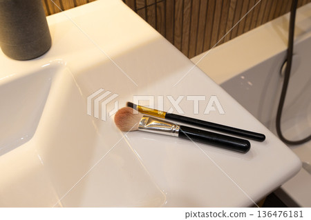 Soft brushes lie on a modern sink, ready for a touch of artistry as natural light fills the stylish bathroom space Soft brushes lie on a modern sink, ready for a touch of artistry as natural light fills the stylish bathroom space 136476181