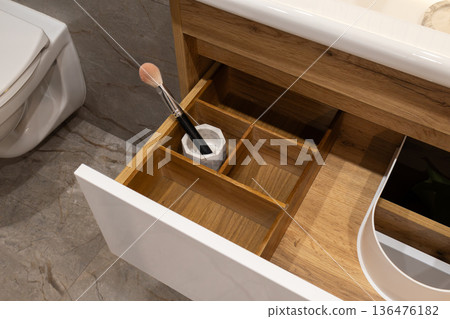 Wooden drawer reveals neatly arranged compartments, showcasing a makeup brush among other beauty essentials in a stylish bathroom 136476182
